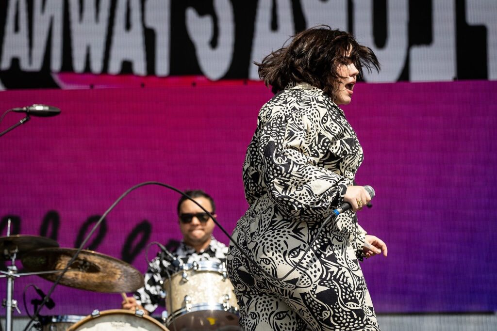 A singer in a patterned jumpsuit performing on an outdoor stage at the Austin City Limits Music Festival in October 2022, with a drummer behind her, a scene near the best hotels near Zilker Park and ACL festival grounds