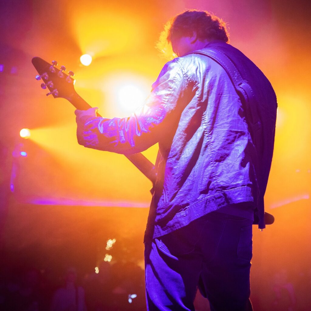 A guitarist playing under bright orange and purple stage lights at 3TEN at ACL Live in Austin