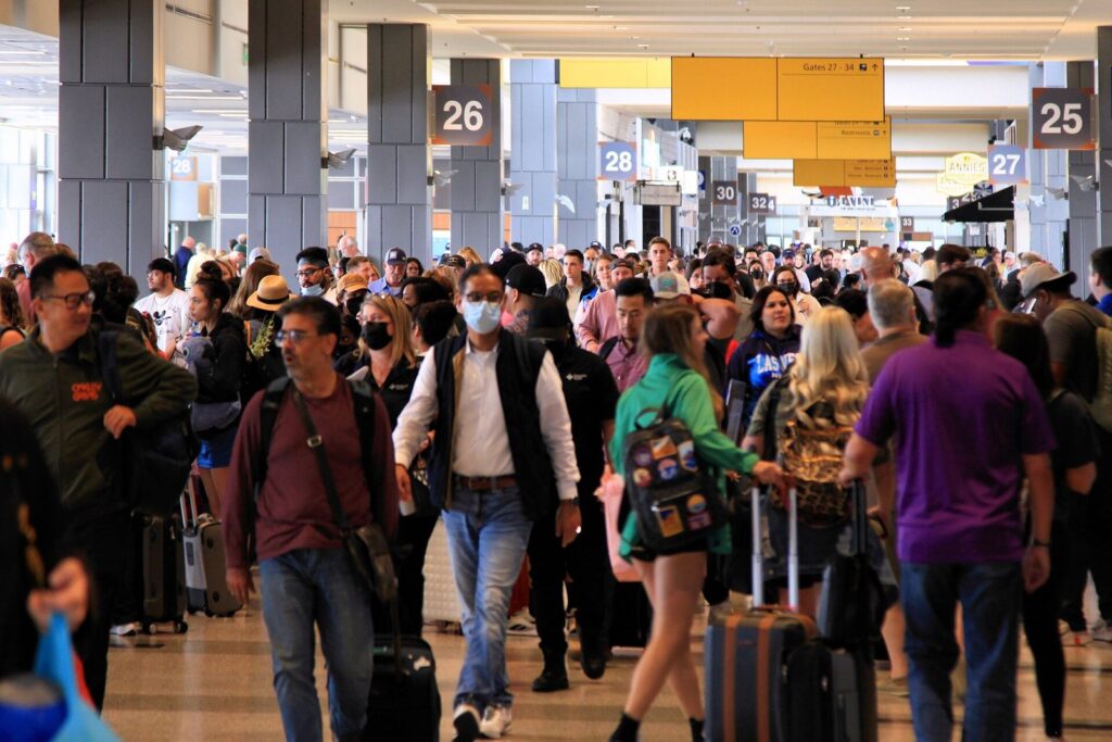 A dense crowd of travelers with roller bags walking past gates 25 and 26 in the Barbara Jordan Terminal at Austin-Bergstrom