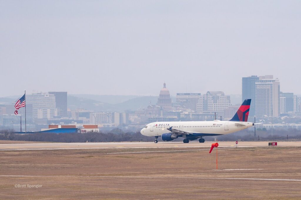 A Delta jet taxiing at Austin-Bergstrom International Airport with the Texas Capitol dome and downtown towers on the horizon