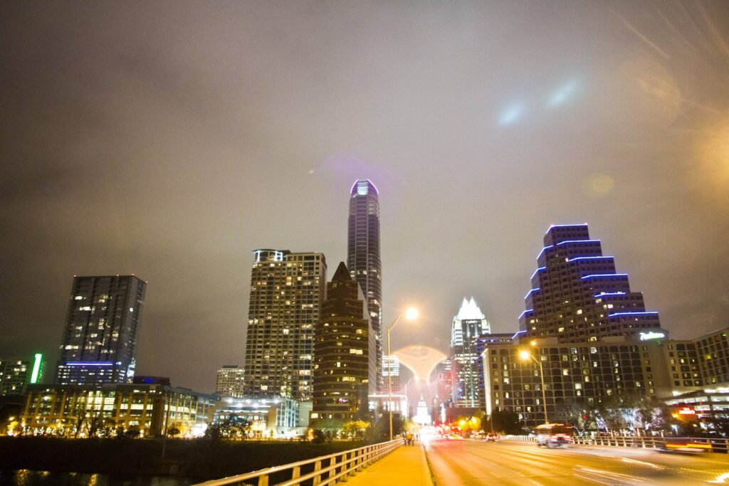 Congress Avenue at night seen from the bridge, with downtown towers lit up and the Texas Capitol at the far end