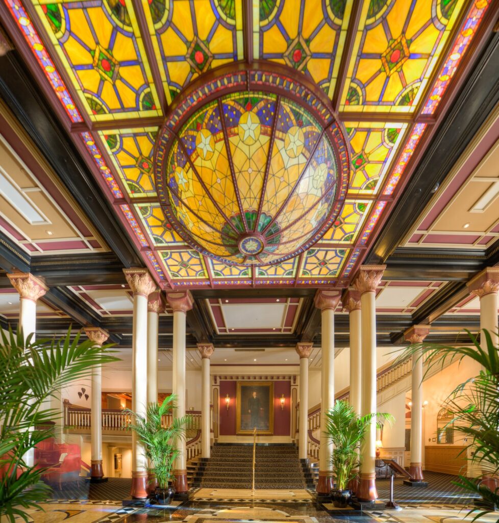 The ornate lobby of the Driskill Hotel in Austin, with marble columns and a glowing stained-glass ceiling dome