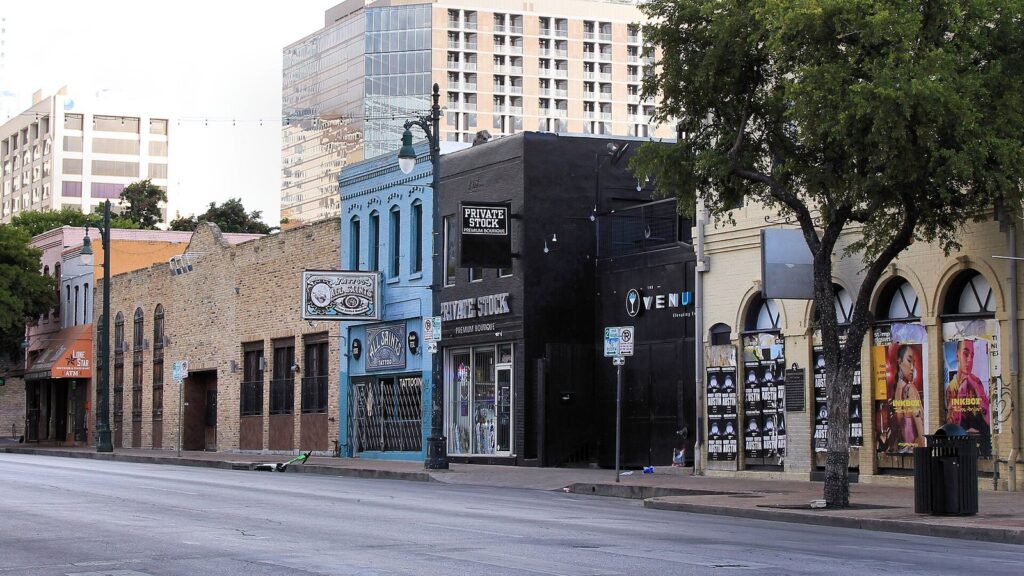Historic two-story brick and stone storefronts on the 500 block of East Sixth Street in downtown Austin, with newer towers behind
