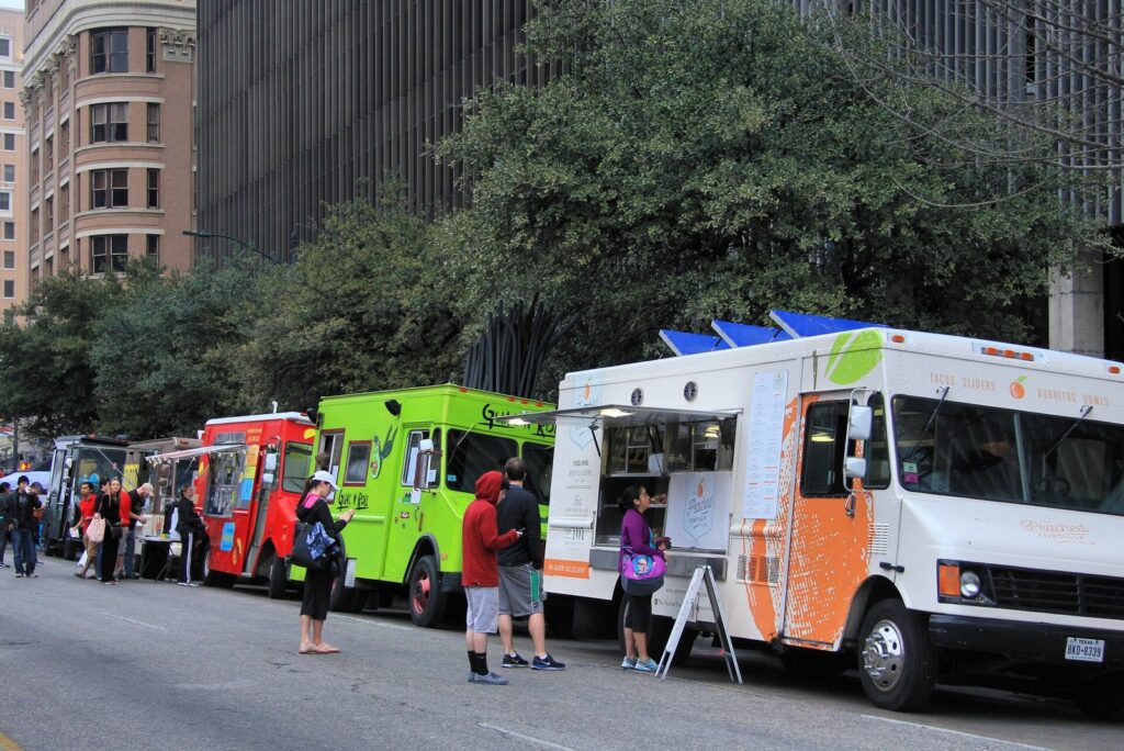 A row of colorful food trucks parked along a downtown Austin street with people ordering at the windows