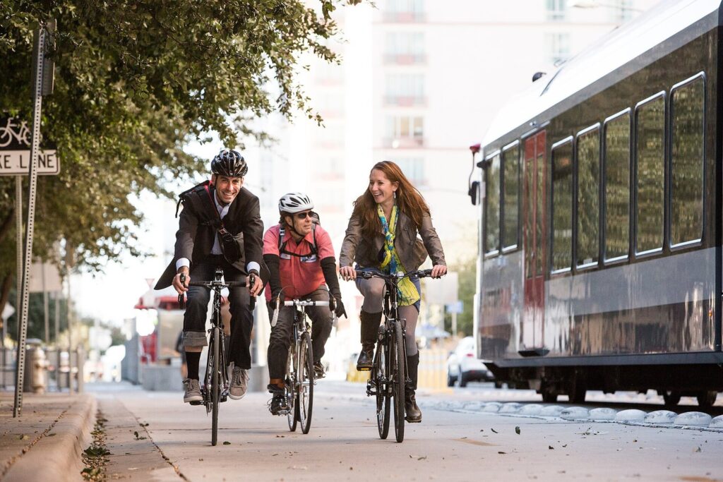 Three cyclists riding side by side in a bump-protected bike lane on Fourth Street in downtown Austin, next to a passing bus