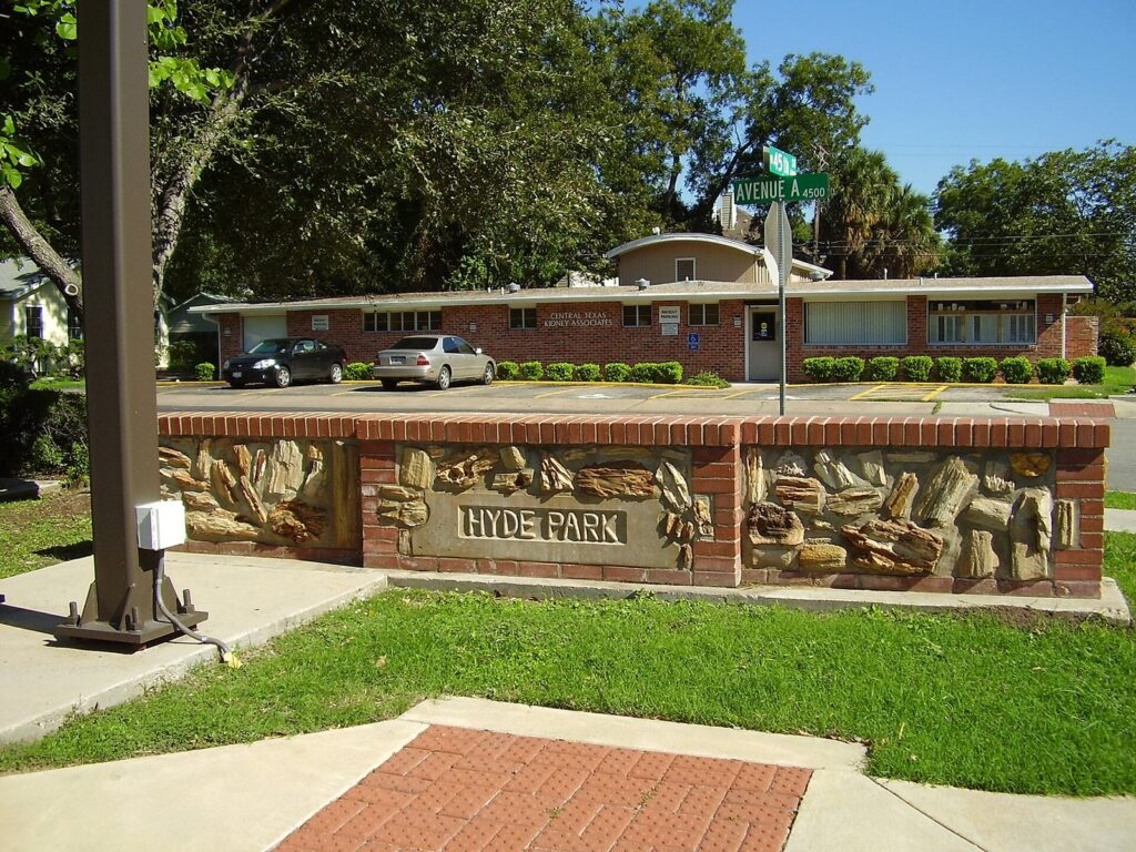 A low brick wall with sculpted relief panels and a Hyde Park sign at a street corner in the Hyde Park neighborhood of Austin