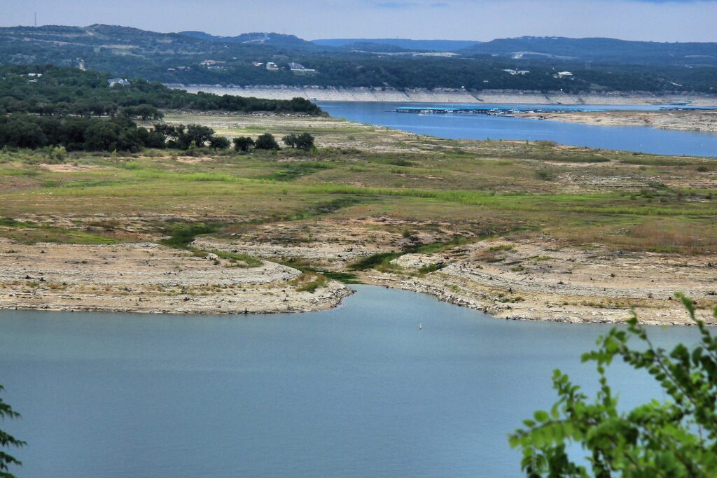 Lake Travis far below its normal level during the 2013 drought, with a wide band of exposed rock and scrub between the water and the tree line