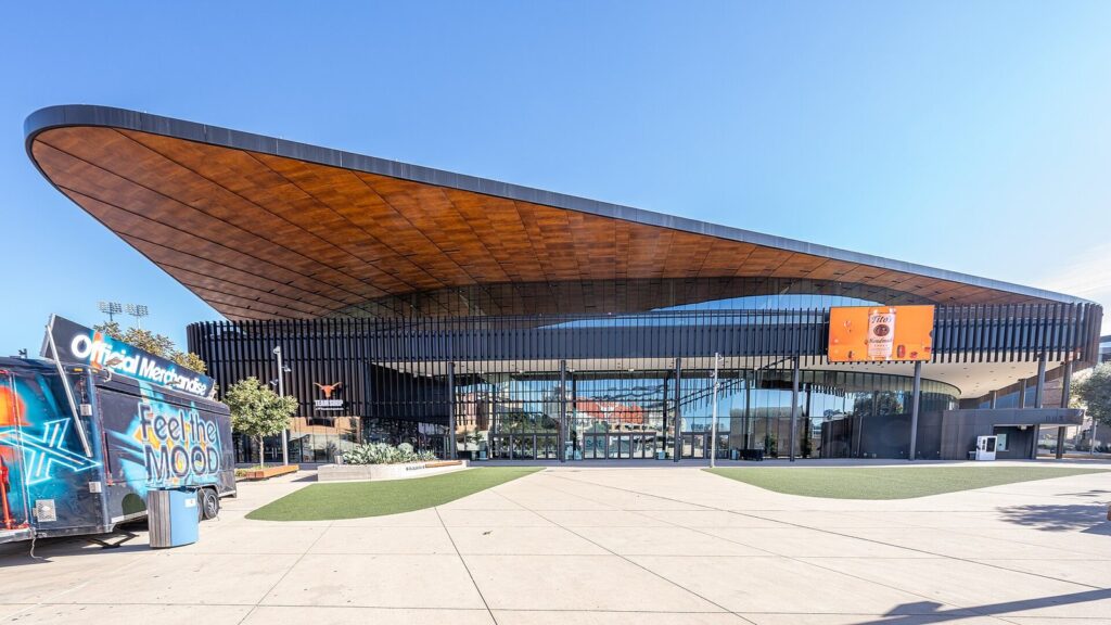 The Moody Center arena at the University of Texas, with its sweeping wood-clad roof overhang above a glass entrance plaza