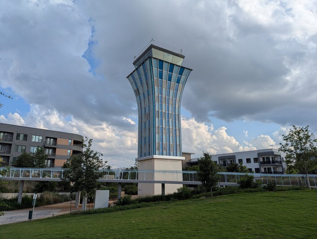 The former Robert Mueller Municipal Airport control tower, a blue-glass tower on a white base, rising over a lawn in the Mueller neighborhood