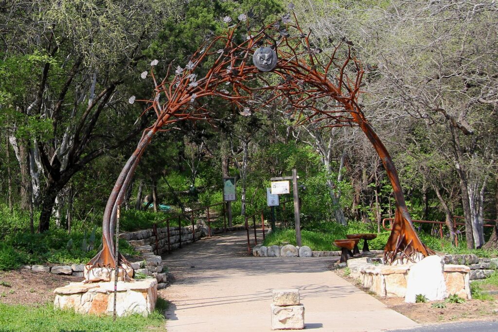 The metal archway entrance to the Austin Nature and Science Center in Zilker Park, framed by trees and limestone