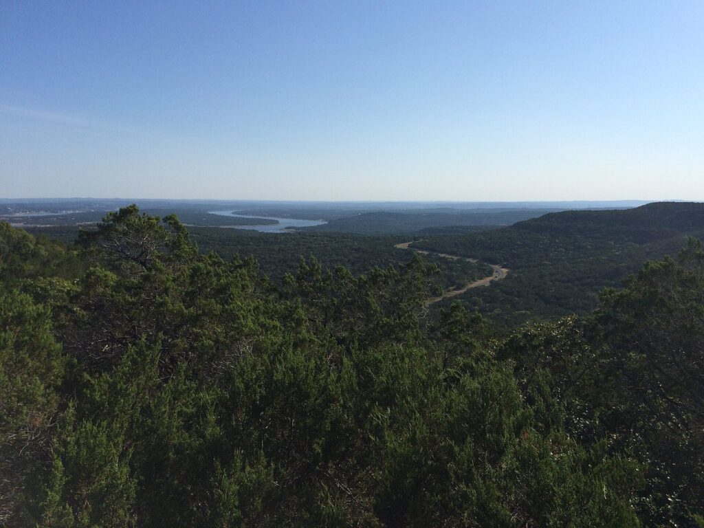 A wooded Hill Country valley near Lago Vista in the Balcones Canyonlands, with ridges fading toward a sliver of Lake Travis