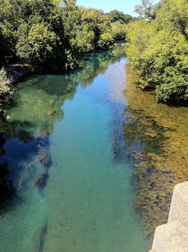 Clear green water in Barton Creek between wooded limestone banks
