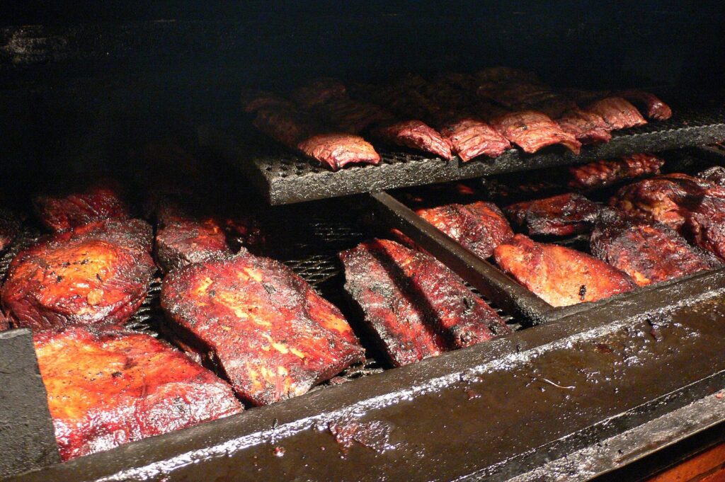 Whole briskets and racks of pork ribs smoking on a large barbecue pit at Black's Barbecue in Lockhart, Texas