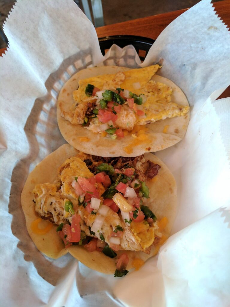 Two egg breakfast tacos in soft flour tortillas topped with pico de gallo in a paper-lined basket