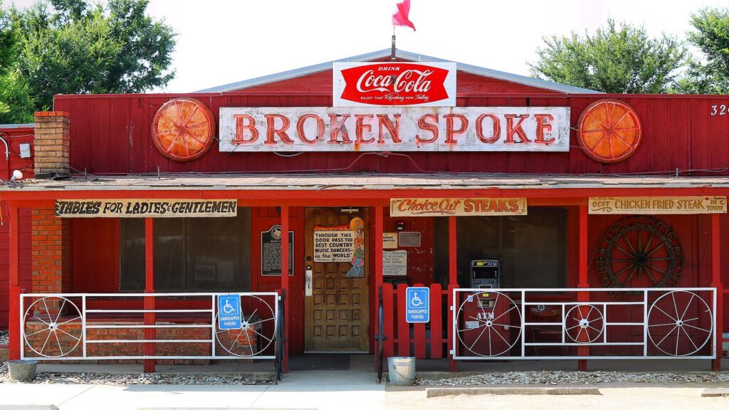 The red wooden front of the Broken Spoke dance hall with its sign, wagon wheels and a Coca-Cola sign on the roof