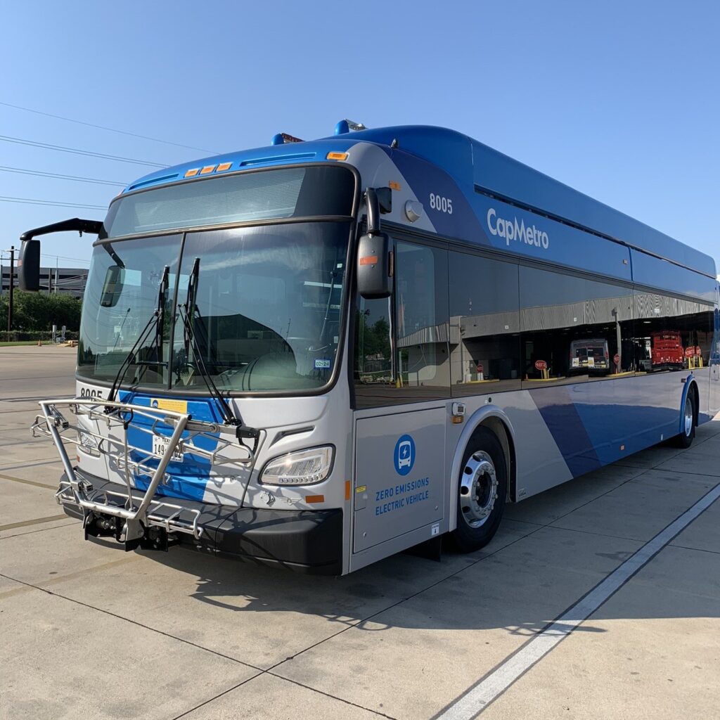 A blue and silver CapMetro electric bus with a front bike rack parked at a transit stop in Austin