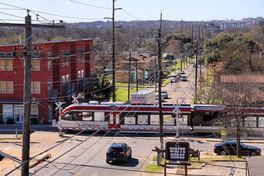 A red and white commuter train crossing Comal Street in East Austin beside the White Horse sign