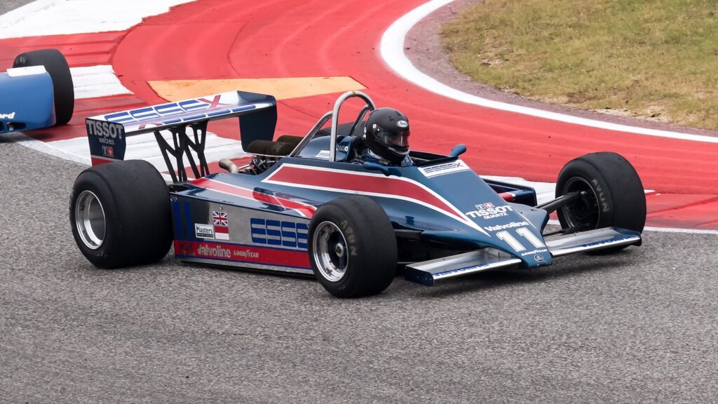 A historic Formula One car in blue, white and red livery cornering on the red and white curbs at Circuit of The Americas