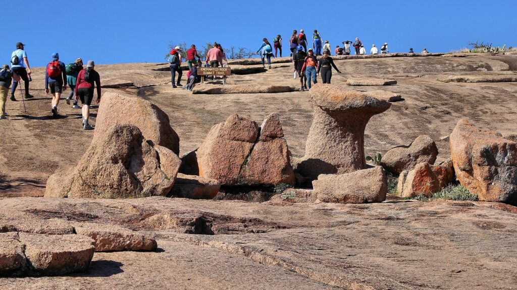 Hikers climbing the pink granite Summit Trail at Enchanted Rock, one of the best Austin vacation ideas for a Hill Country weekend