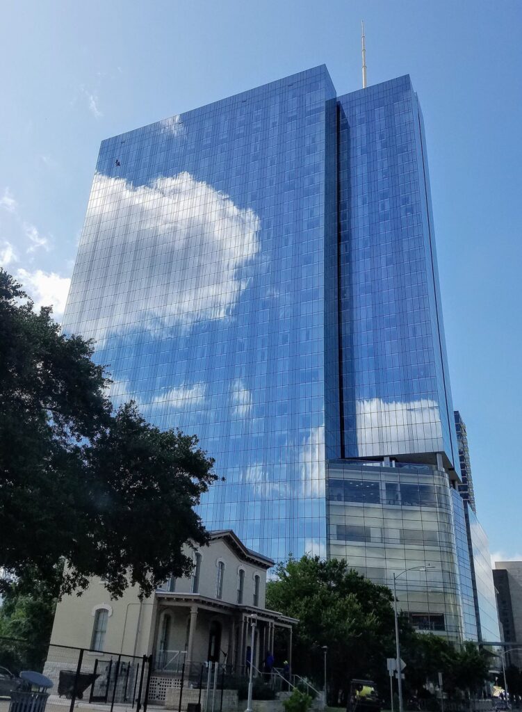 The Fairmont Austin's tall blue glass tower rising above a historic house and trees in downtown Austin