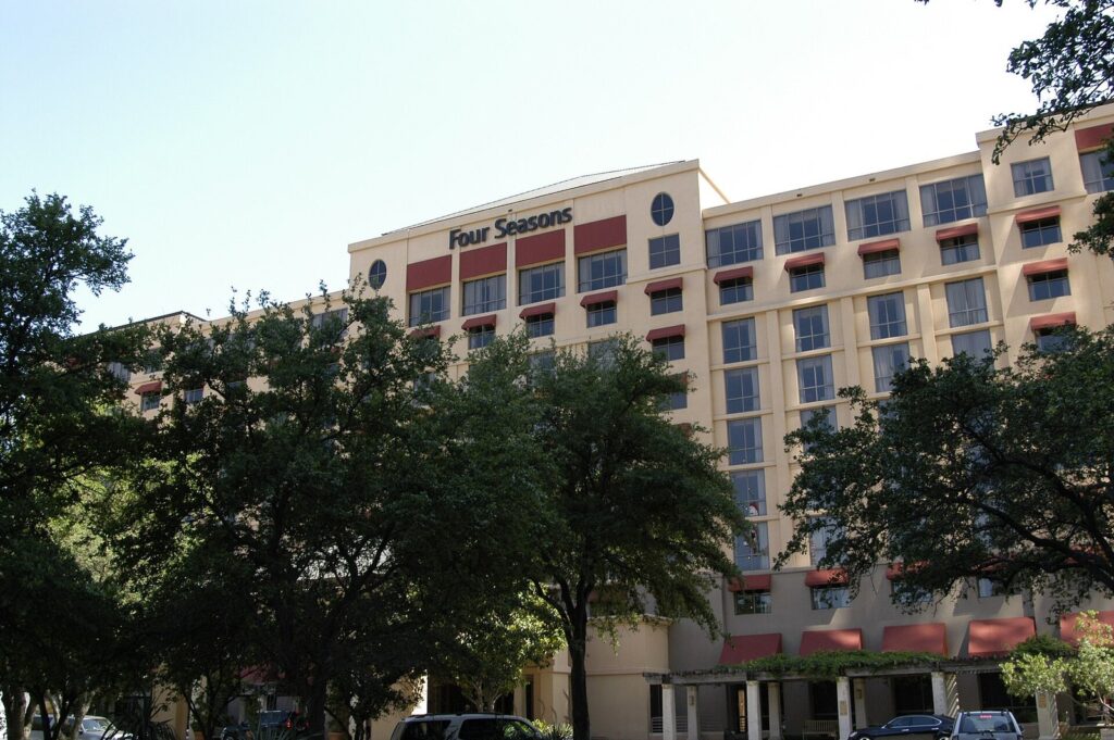 The Four Seasons Hotel Austin's cream-colored facade with red awnings, framed by live oak trees downtown, one of the best luxury hotels in Austin