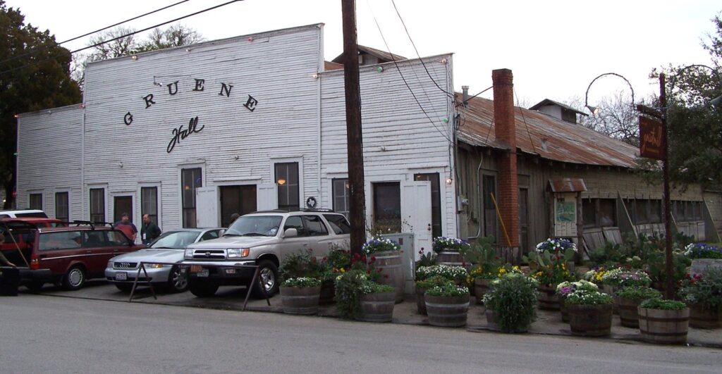 The white clapboard front of Gruene Hall dance hall with its painted sign, parked cars and potted flowers