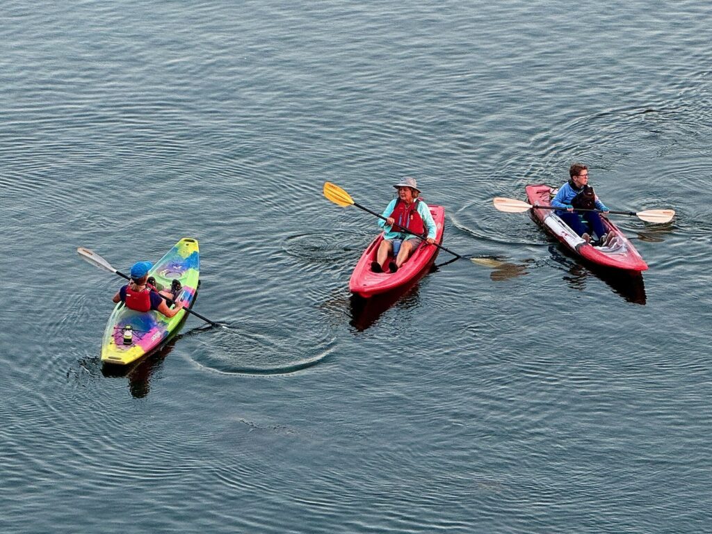 Three paddlers in life jackets in colorful kayaks on the calm water of Lady Bird Lake, a morning outing near the family friendly hotels in Austin