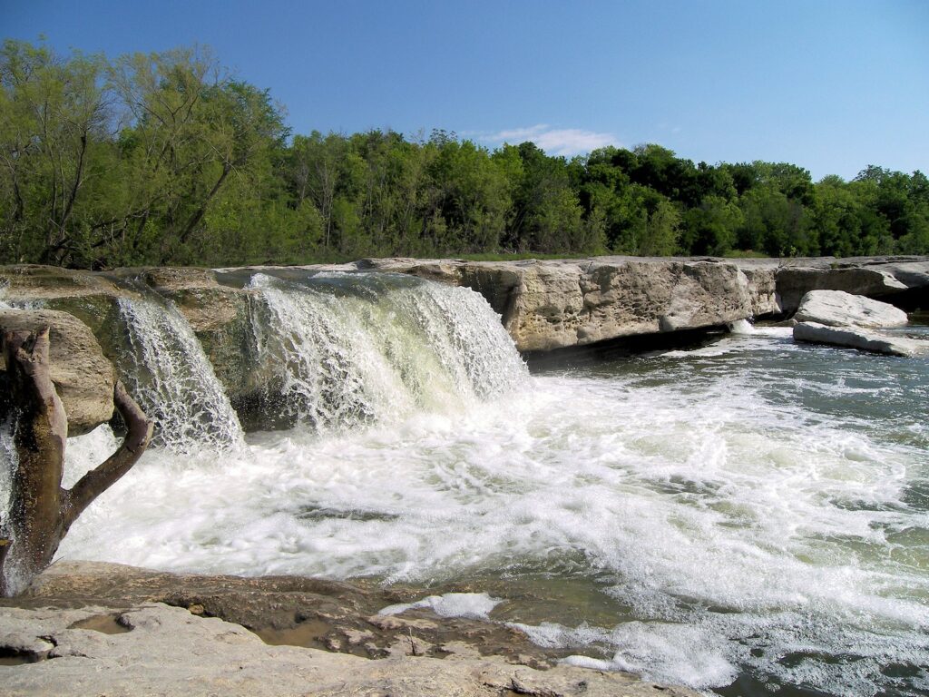 White water pouring over limestone ledges at McKinney Falls State Park under a clear blue sky