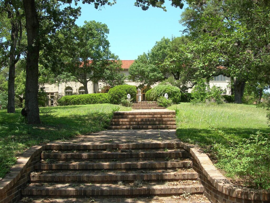 Brick steps rising through a green lawn under oak trees toward the Italianate mansion at the Perry estate in central Austin