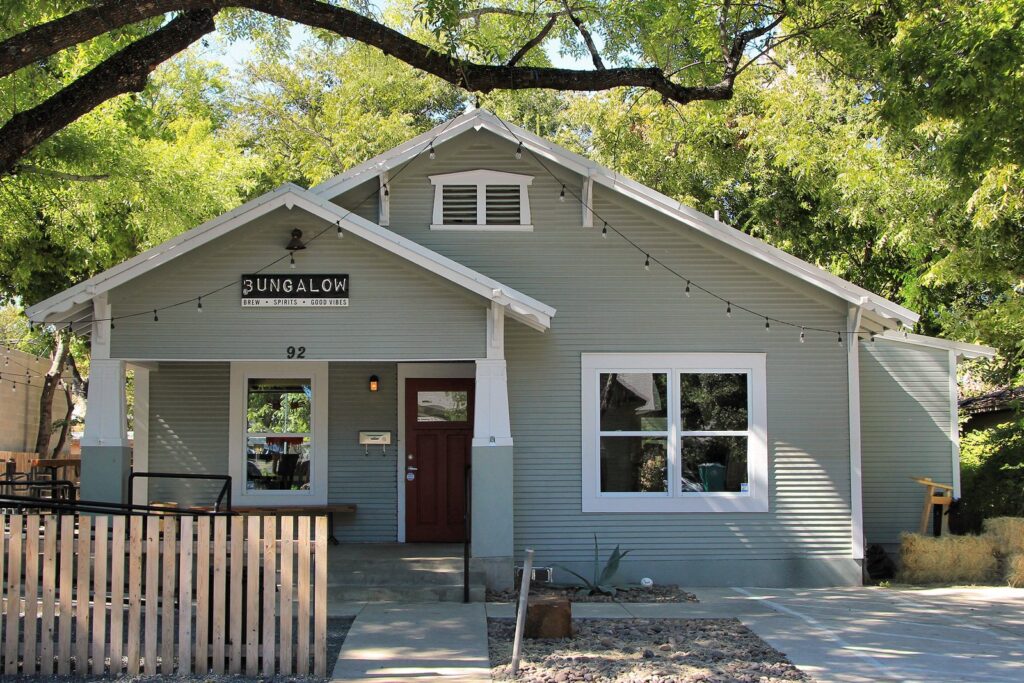 A converted wooden bungalow with a porch and string lights, now a bar on Rainey Street under large shade trees
