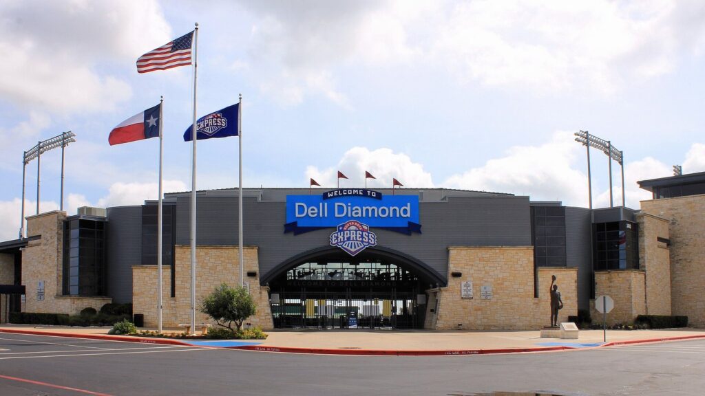 The southwest entrance of the Dell Diamond in Round Rock, with flags flying above the stone-and-steel gate of the ballpark