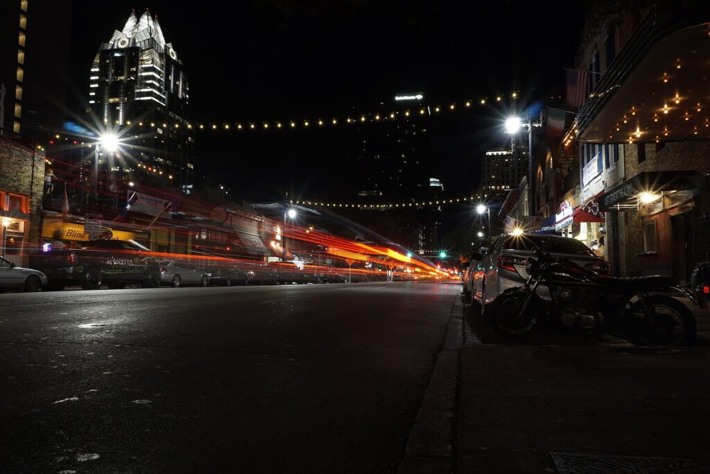 Sixth Street at night with streaks of car lights, string lights overhead and the lit Frost Bank Tower behind