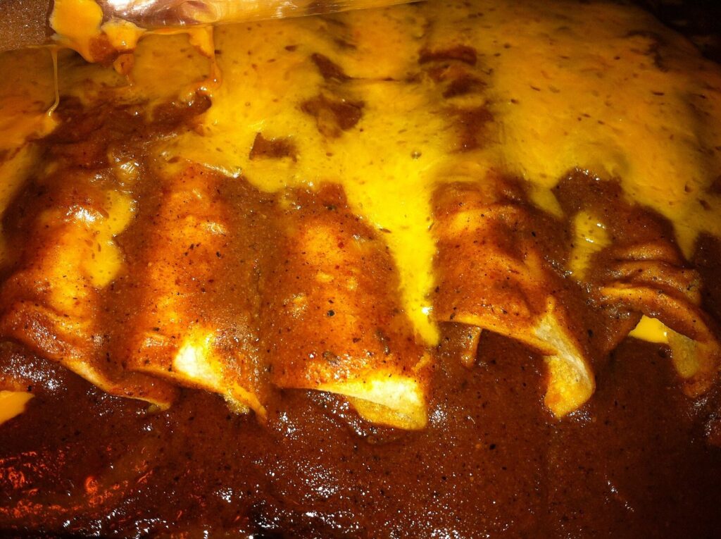 Cheese enchiladas covered in melted yellow cheese and dark red chili gravy on a plate
