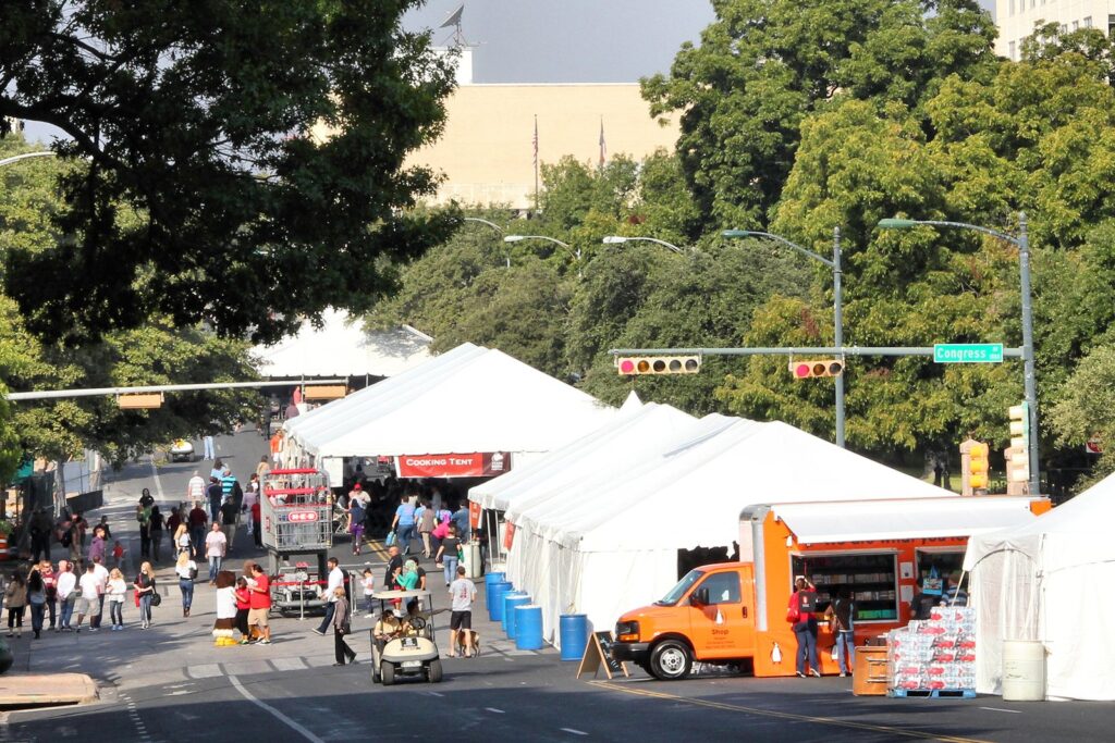 White festival tents lining a downtown street near the Texas Capitol during the Texas Book Festival, with visitors walking between them