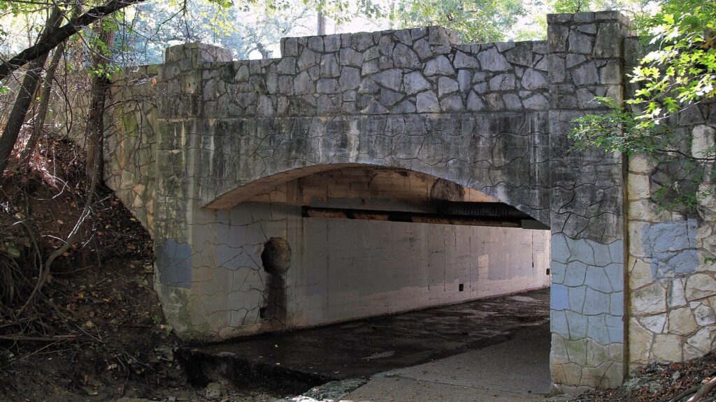A rustic stone vehicle bridge over a wooded creek in the Travis Heights and Fairview Park historic district of South Austin