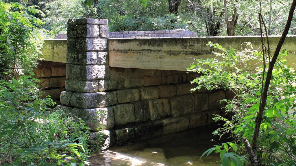 A stone bridge abutment over Turkey Creek, surrounded by green woods at Emma Long Metropolitan Park
